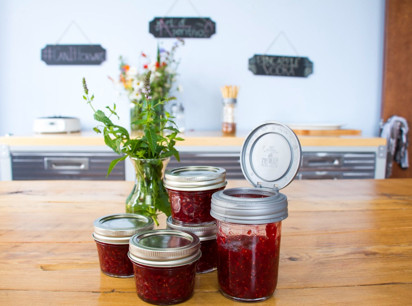A collection of jars with jelly and jam. One is topped with a reCAP® Regular Mouth Mason Jar FLIP Top Lid