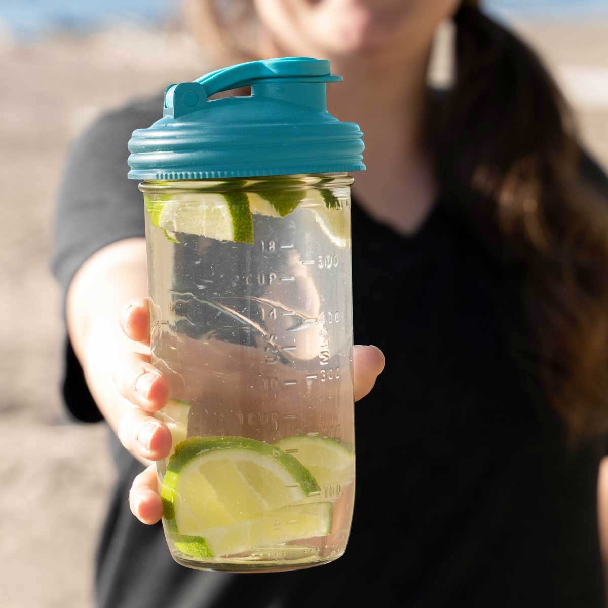 Person holding up glass water bottle made from Mason Jar and Mason Jar POUR lid.