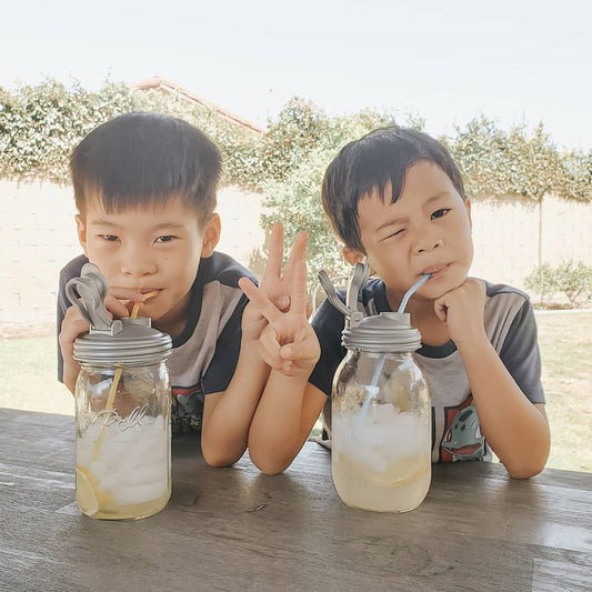 Two kids drinking from Mason jars with POUR lids