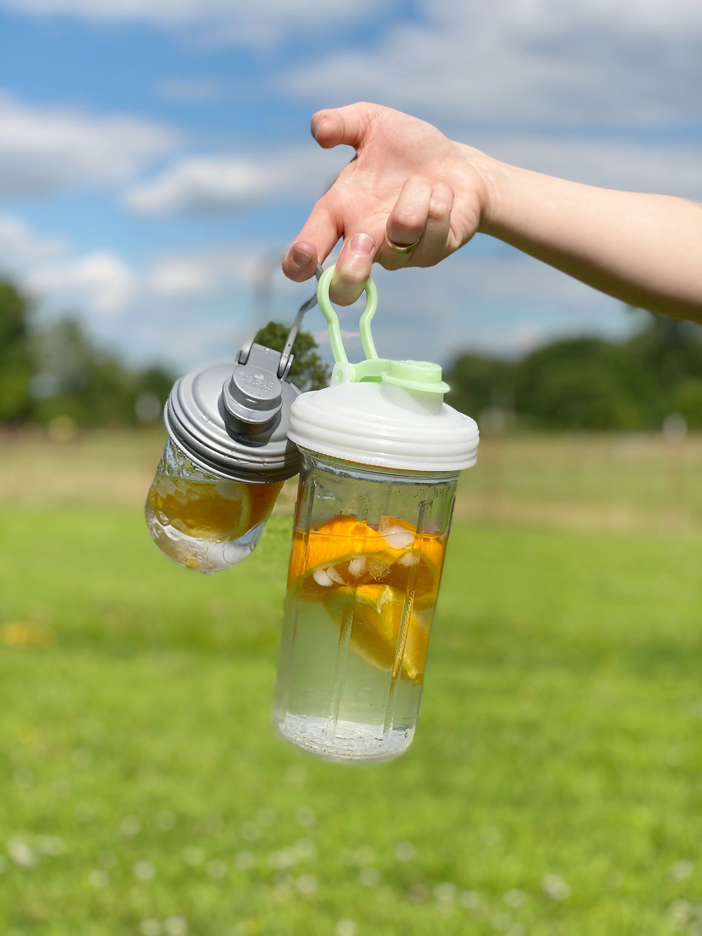 A person holding up two Mason jars that they've turned into glass water bottles by using the POUR lid.