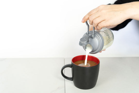 Person pouring half and half from a mason jar with a silver Mason Jar POUR Lid.